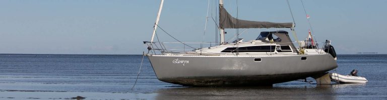 De grijze Eowyn drooggevallen op het wad, met de rubberboot ernaast