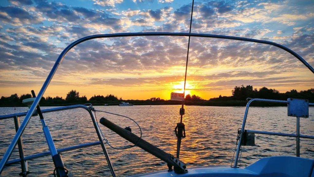 Zonsondergang boven het Lauwersmeer, gezien over de preekstoel van de Eowyn; een motorboot in de verte, bomen aan de horizon.