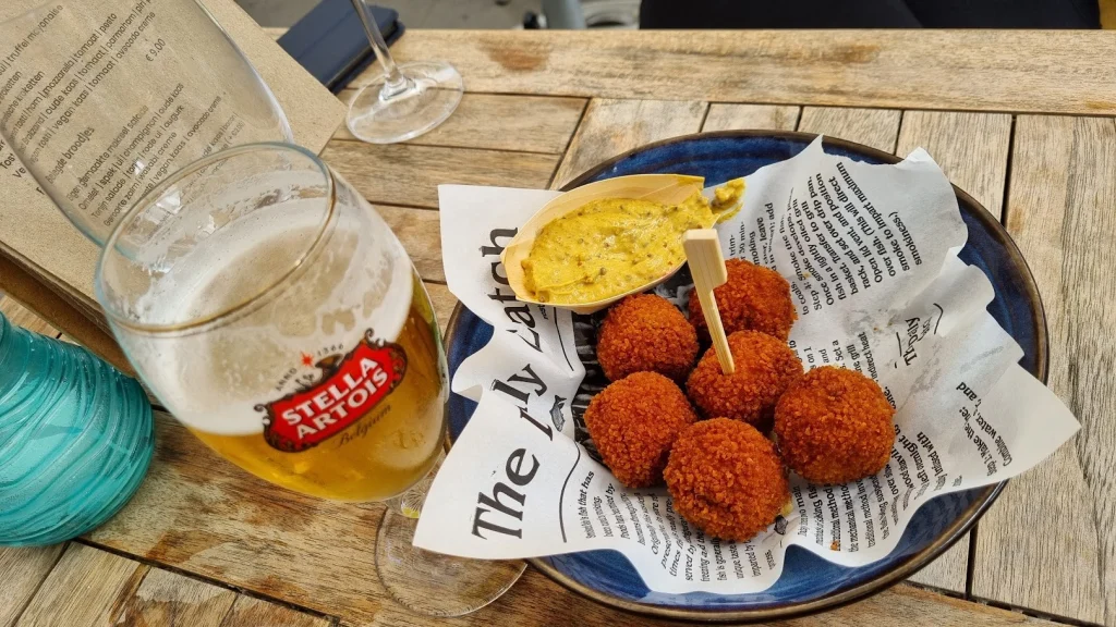Bitterballen met mosterd op een blauw bord en een glas bier op een houten terrastafel op Schiermonnikoog.