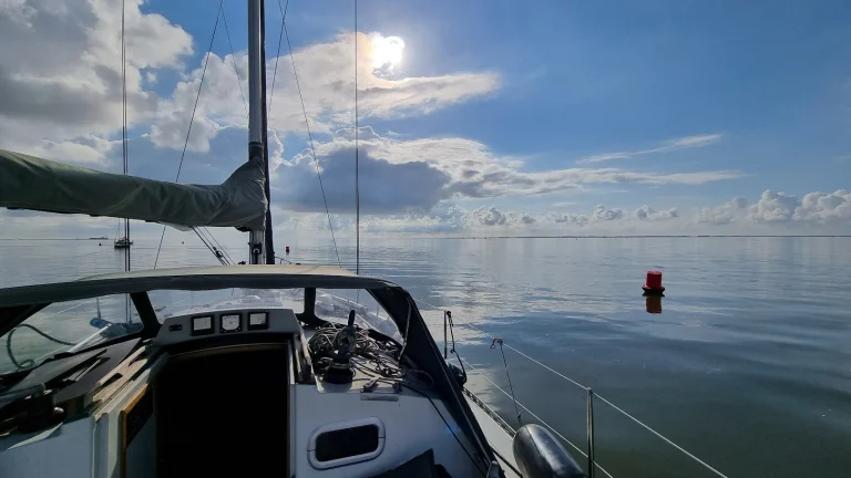 Spiegelglad wad onder een blauwe lucht met stapelwolken, gezien vanuit de kuip van de Eowyn; een rode ton in het water en een andere zeilboot in de verte.