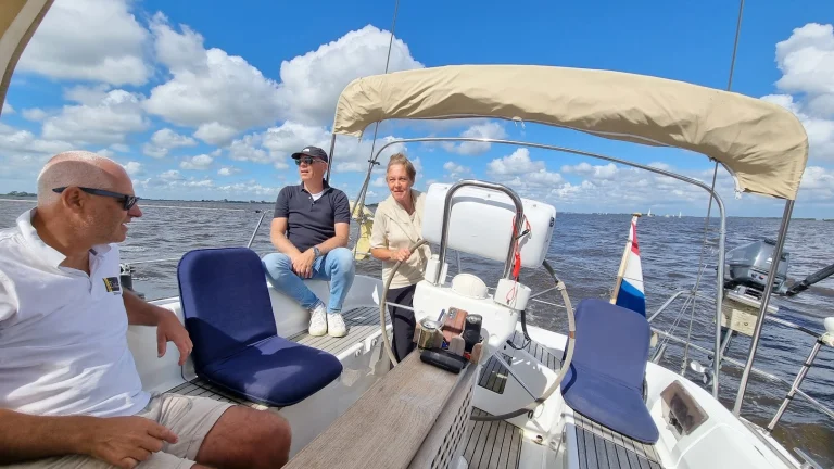 In de kuip van een Feeling 446di: moeder aan het stuurwiel, twee mannen met zonnebril op de bankjes, de Nederlandse vlag op het hek; blauwe lucht met stapelwolken boven een breed meer.