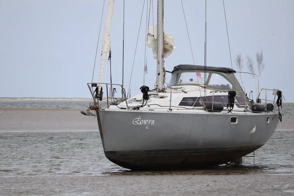 De Eowyn staat drooggevallen op een zandplaat op het wad, met wat water om de kiel en een grijze lucht.