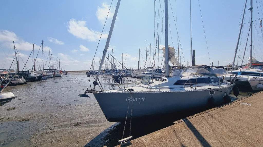 De Eowyn ligt bij laag water aan een betonnen kade in een jachthaven vol zeilboten, de bodem van de haven ligt deels droog; zonnige lucht.