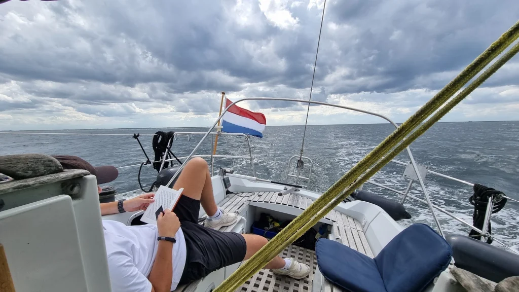 Mijn neefje ligt languit in de kuip een boek te lezen terwijl de Eowyn over een grijze, onstuimige Noordzee vaart; de Nederlandse vlag waait op het hek onder donkere wolken.