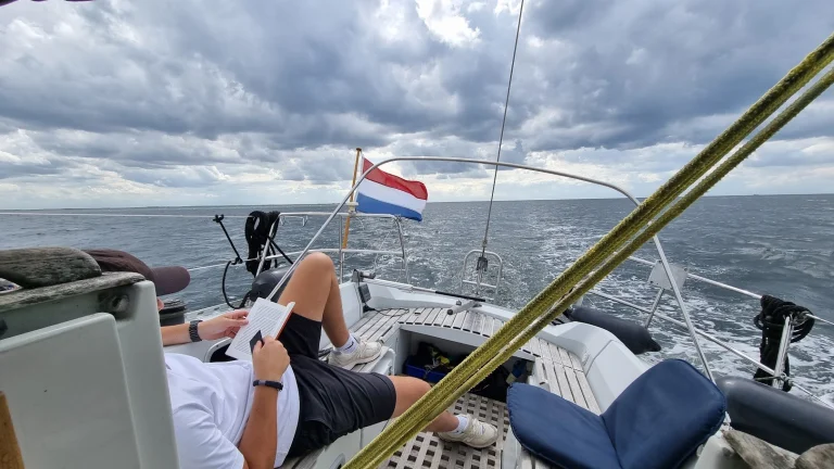 Mijn neefje ligt languit in de kuip een boek te lezen terwijl de Eowyn over een grijze, onstuimige Noordzee vaart; de Nederlandse vlag waait op het hek onder donkere wolken.
