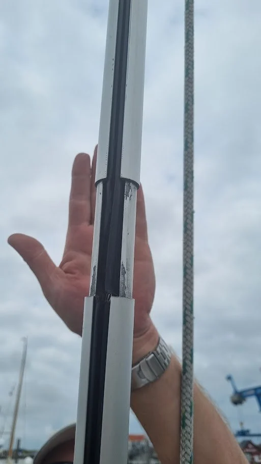 Close-up van het aluminium rolfokprofiel, waarvan twee delen uit elkaar zijn geschoven zodat het voorlijk van het zeil zichtbaar is; een hand erachter voor de maat.
