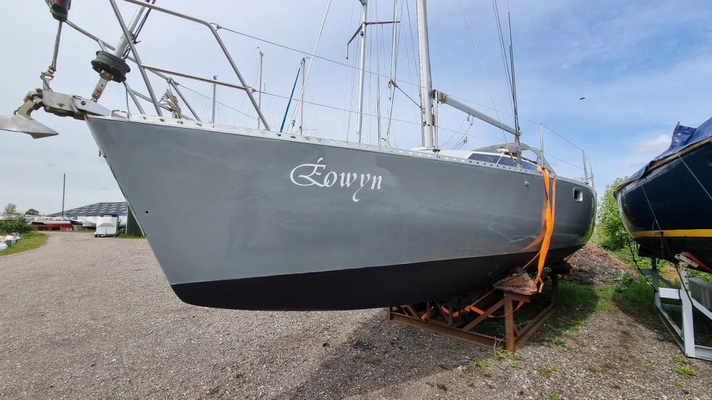 De Eowyn op de bok op het werfterrein, van voren gezien: de grijze romp glimt na het poetsen, met de sierlijke witte naam Éowyn op de boeg en een vers geschilderde donkere antifouling-onderkant, onder een blauwe lucht met wolkjes.
